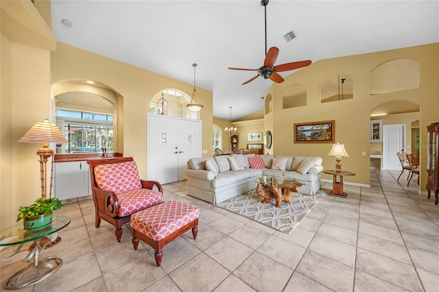 living area featuring high vaulted ceiling, ceiling fan with notable chandelier, visible vents, and light tile patterned flooring