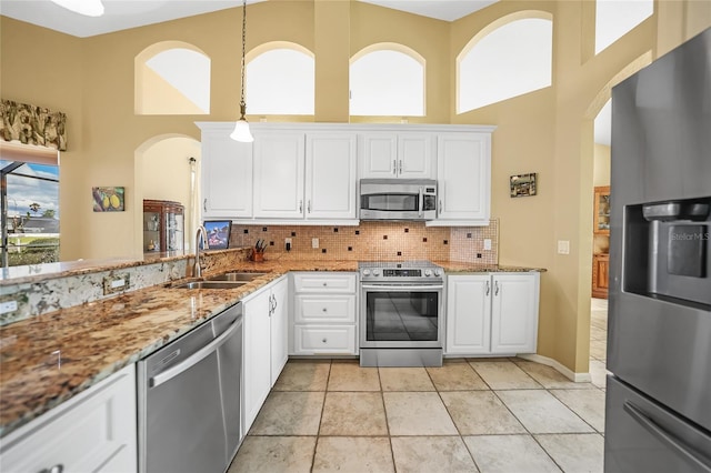 kitchen with a towering ceiling, appliances with stainless steel finishes, decorative backsplash, and a sink