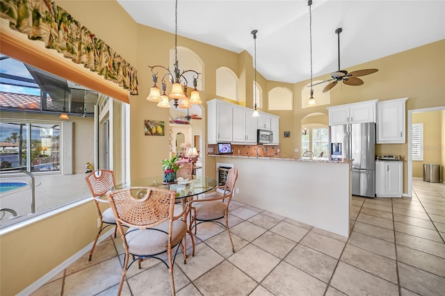 dining room featuring light tile patterned floors, baseboards, arched walkways, a towering ceiling, and ceiling fan with notable chandelier