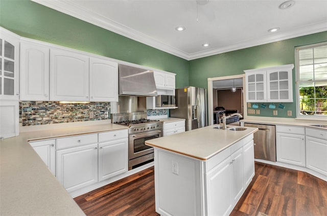 kitchen with crown molding, a sink, appliances with stainless steel finishes, glass insert cabinets, and wall chimney range hood