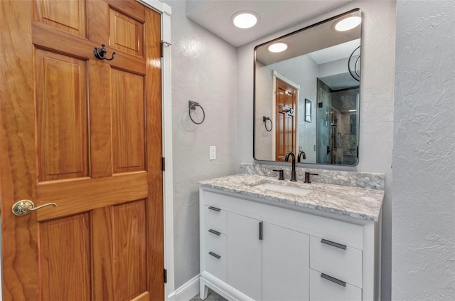 bathroom featuring vanity, a textured wall, baseboards, and a shower with door