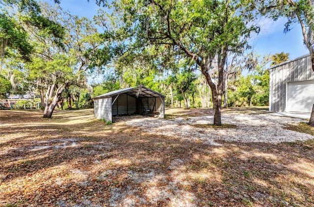 view of yard featuring an outdoor structure, a carport, dirt driveway, and an outbuilding