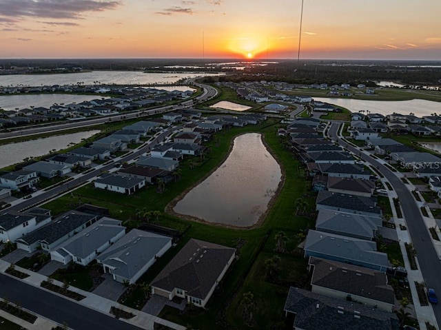 aerial view at dusk with a water view and a residential view