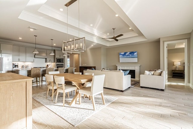 dining space featuring a raised ceiling, a ceiling fan, wood tiled floor, crown molding, and a fireplace