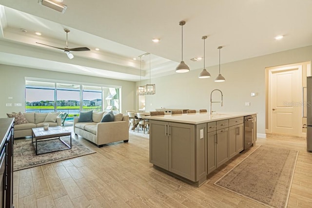 kitchen featuring a sink, open floor plan, light countertops, a tray ceiling, and a center island with sink