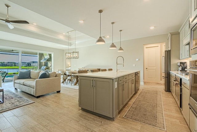 kitchen with open floor plan, a kitchen island with sink, light countertops, pendant lighting, and a sink