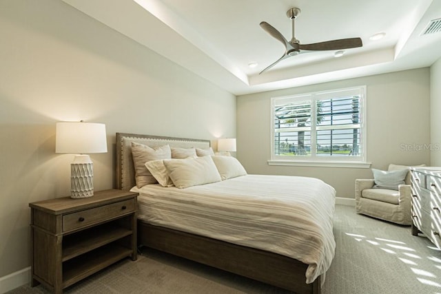 carpeted bedroom featuring ceiling fan, a raised ceiling, visible vents, and baseboards