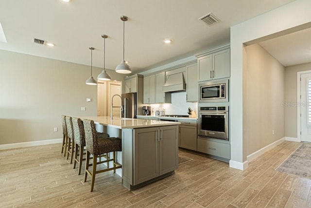 kitchen featuring visible vents, hanging light fixtures, a kitchen island with sink, stainless steel appliances, and light countertops