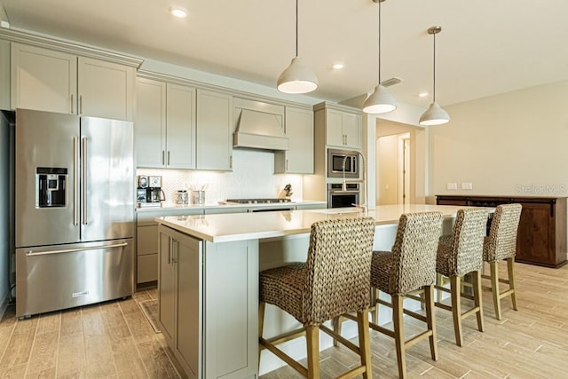 kitchen featuring a spacious island, light countertops, hanging light fixtures, appliances with stainless steel finishes, and premium range hood