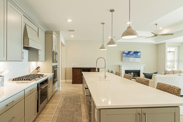 kitchen featuring a sink, light countertops, appliances with stainless steel finishes, custom exhaust hood, and a center island with sink