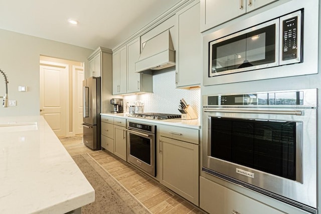 kitchen with light stone counters, stainless steel appliances, premium range hood, light wood finished floors, and tasteful backsplash