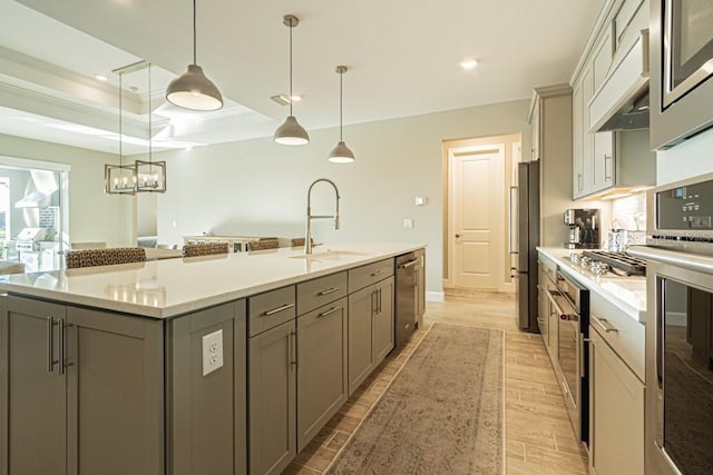 kitchen with decorative light fixtures, gray cabinetry, appliances with stainless steel finishes, a sink, and a large island with sink