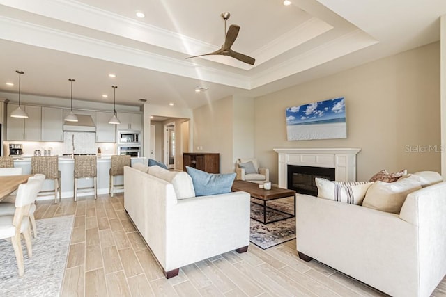 living room featuring recessed lighting, a raised ceiling, a ceiling fan, wood tiled floor, and a glass covered fireplace