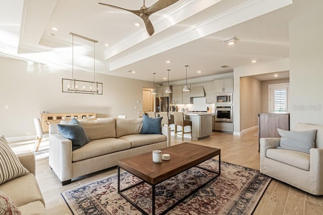 living room featuring ornamental molding, light wood-type flooring, a raised ceiling, and baseboards