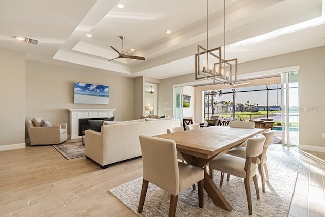 dining room featuring light wood-style flooring, visible vents, baseboards, a raised ceiling, and a glass covered fireplace