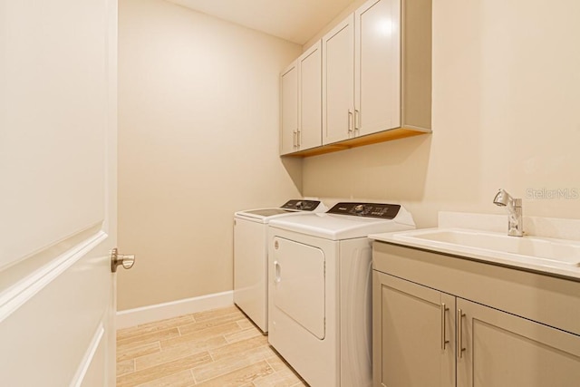 laundry room with cabinet space, baseboards, washer and clothes dryer, wood finish floors, and a sink