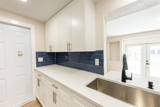 kitchen with light countertops, backsplash, a sink, and white cabinets