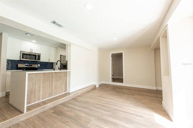 kitchen featuring light wood finished floors, appliances with stainless steel finishes, visible vents, and tasteful backsplash