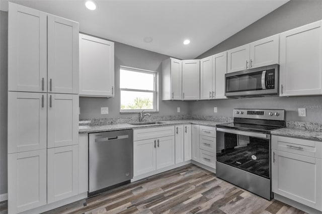 kitchen featuring white cabinets, lofted ceiling, appliances with stainless steel finishes, wood finished floors, and a sink