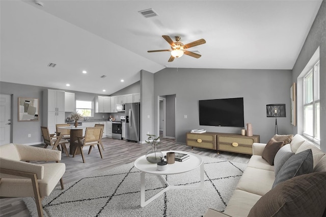 living room featuring light wood-style flooring, visible vents, vaulted ceiling, and a ceiling fan