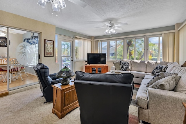 living area with a ceiling fan, light carpet, a textured wall, and a textured ceiling