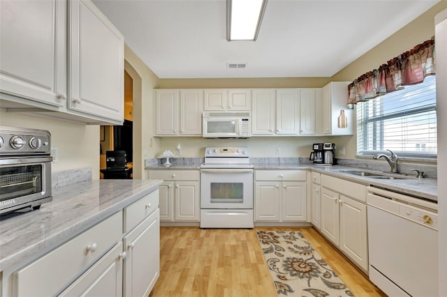 kitchen with white appliances, a sink, visible vents, light wood-style floors, and white cabinets