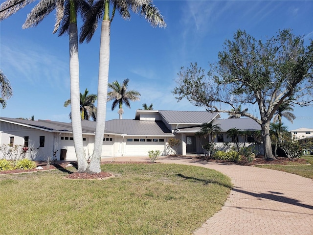 view of front of home featuring an attached garage, a front lawn, metal roof, and decorative driveway