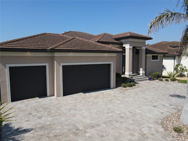 prairie-style home featuring a tiled roof, decorative driveway, an attached garage, and stucco siding