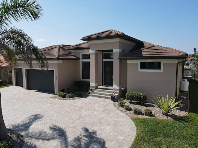 prairie-style home with an attached garage, a tile roof, decorative driveway, and stucco siding