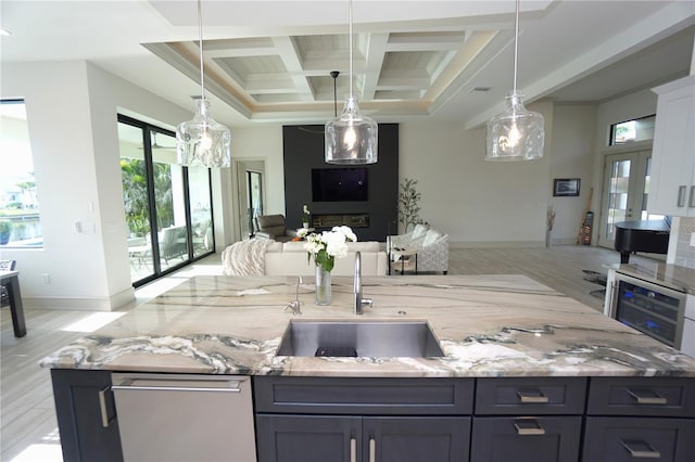 kitchen featuring coffered ceiling, light stone counters, open floor plan, decorative light fixtures, and a sink