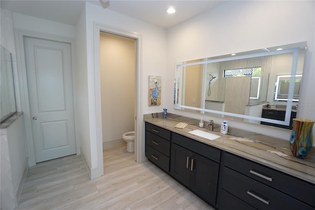 bathroom featuring toilet, recessed lighting, wood finished floors, vanity, and a tile shower