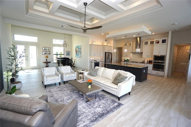 living area with crown molding, a high ceiling, coffered ceiling, and light wood-style floors