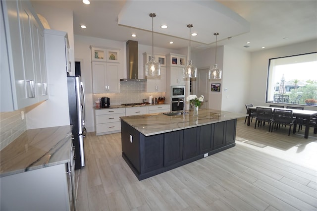 kitchen featuring wall chimney exhaust hood, light wood-type flooring, white cabinetry, and stainless steel appliances