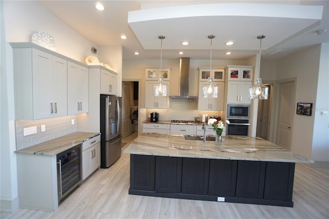 kitchen with beverage cooler, white cabinetry, appliances with stainless steel finishes, wall chimney exhaust hood, and washer / clothes dryer