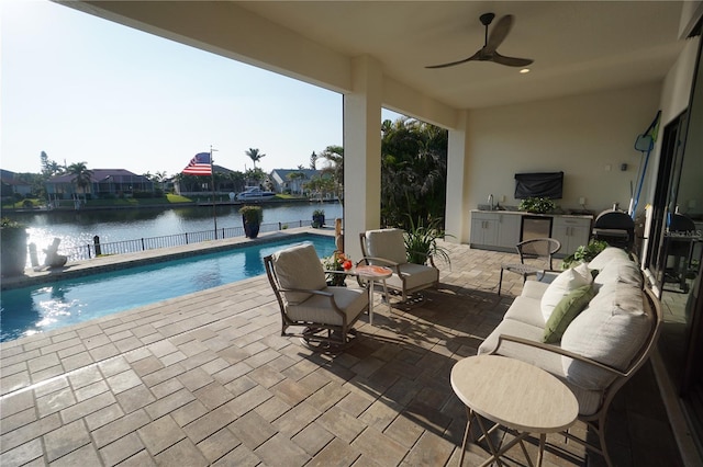 view of patio featuring an outdoor pool, a ceiling fan, a water view, fence, and a sink