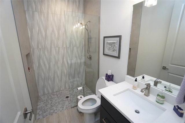 bathroom featuring toilet, wood finished floors, a tile shower, and vanity