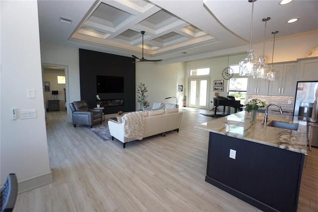 living room with french doors, visible vents, light wood-style flooring, a high ceiling, and coffered ceiling