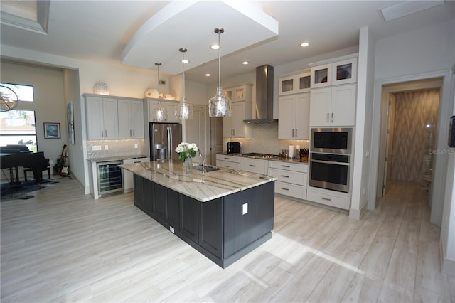 kitchen with beverage cooler, appliances with stainless steel finishes, decorative backsplash, wall chimney exhaust hood, and light wood finished floors