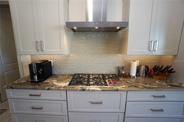 kitchen with stone counters, stainless steel gas stovetop, decorative backsplash, white cabinets, and wall chimney range hood