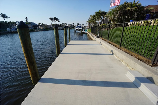 dock area featuring a water view, fence, and a lawn