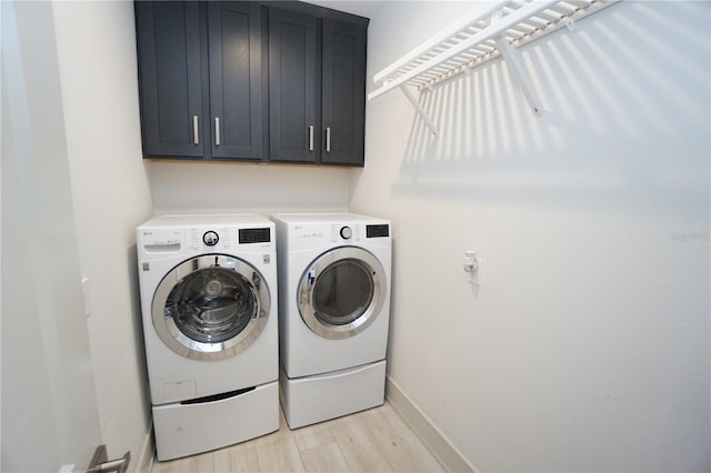 clothes washing area featuring light wood-style flooring, washing machine and clothes dryer, cabinet space, and baseboards