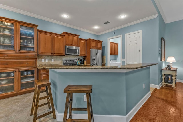 kitchen with a breakfast bar, brown cabinets, crown molding, backsplash, and appliances with stainless steel finishes