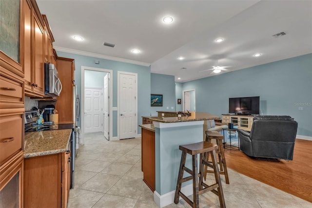 kitchen with visible vents, a kitchen breakfast bar, ornamental molding, appliances with stainless steel finishes, and brown cabinetry