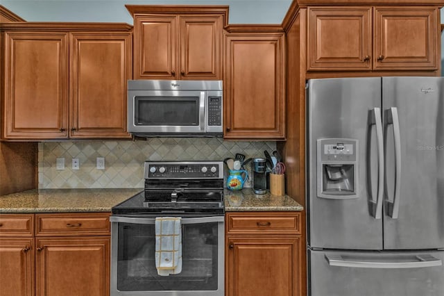 kitchen featuring stainless steel appliances, brown cabinets, dark stone countertops, and decorative backsplash