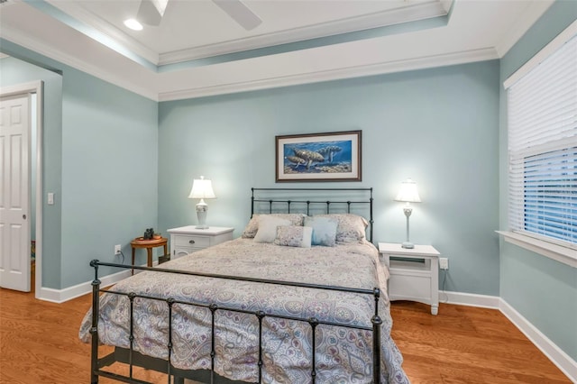 bedroom featuring baseboards, ornamental molding, a raised ceiling, and wood finished floors