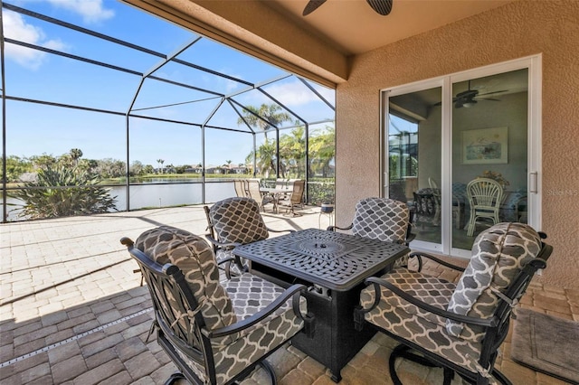 view of patio / terrace with a ceiling fan, outdoor dining space, glass enclosure, and a water view