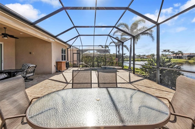 view of patio / terrace featuring a ceiling fan, glass enclosure, and a water view