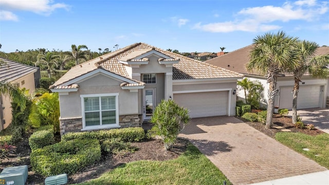 mediterranean / spanish-style home featuring decorative driveway, stucco siding, a garage, stone siding, and a tiled roof