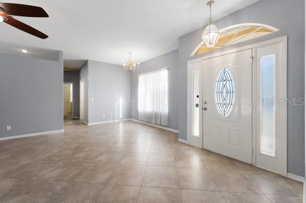 entryway with ceiling fan with notable chandelier, baseboards, and light tile patterned floors