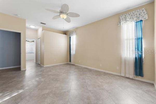 unfurnished room with baseboards, visible vents, and a ceiling fan